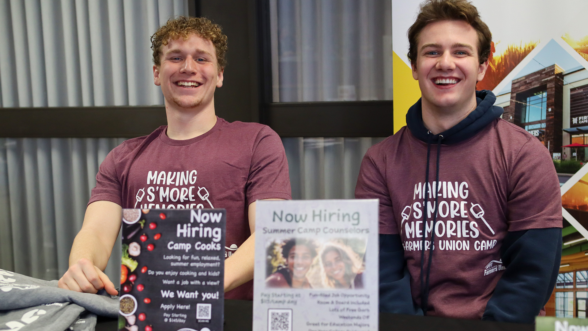 2 males sit at a table recruiting students to become summer camp counselors