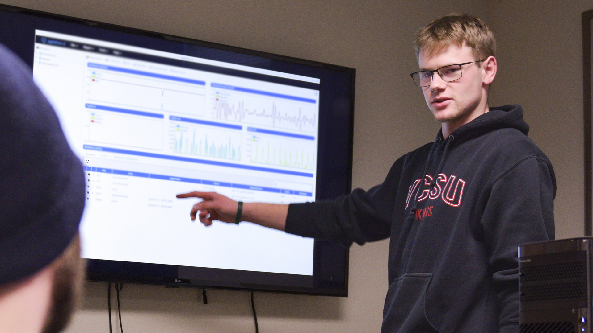 A student points to a TV screen showing a presentation of data.