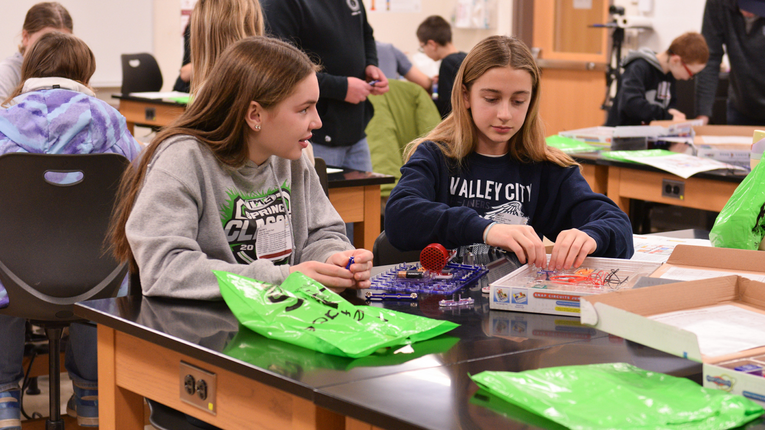 2 Junior high girls sit at a table and work with electricity experiments.