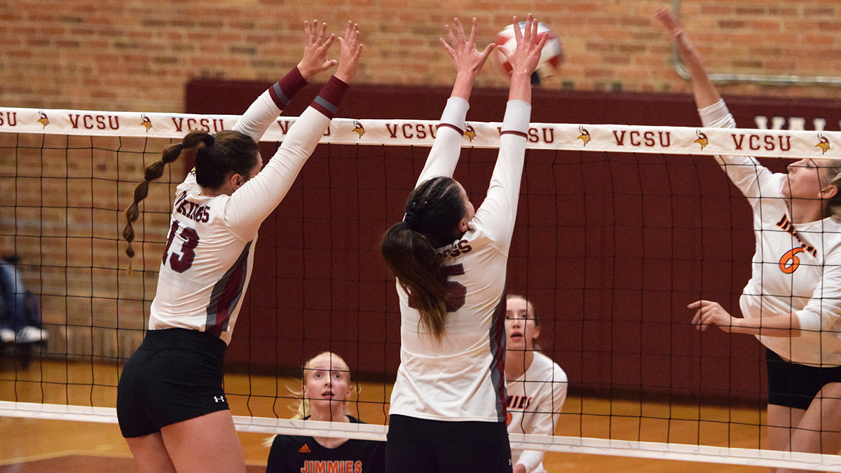 Two VCSU volleyball athletes block at the net against opponents