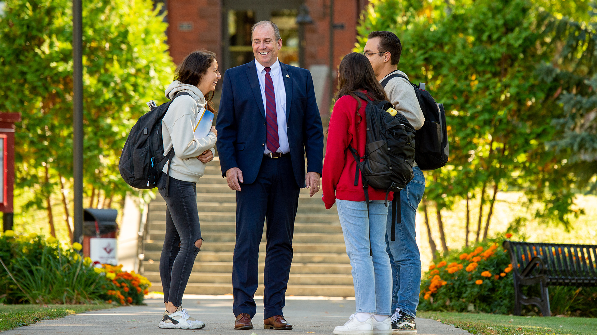 VCSU president Alan LaFave talks with 3 students on the sidewalk in front of McFarland Hall.