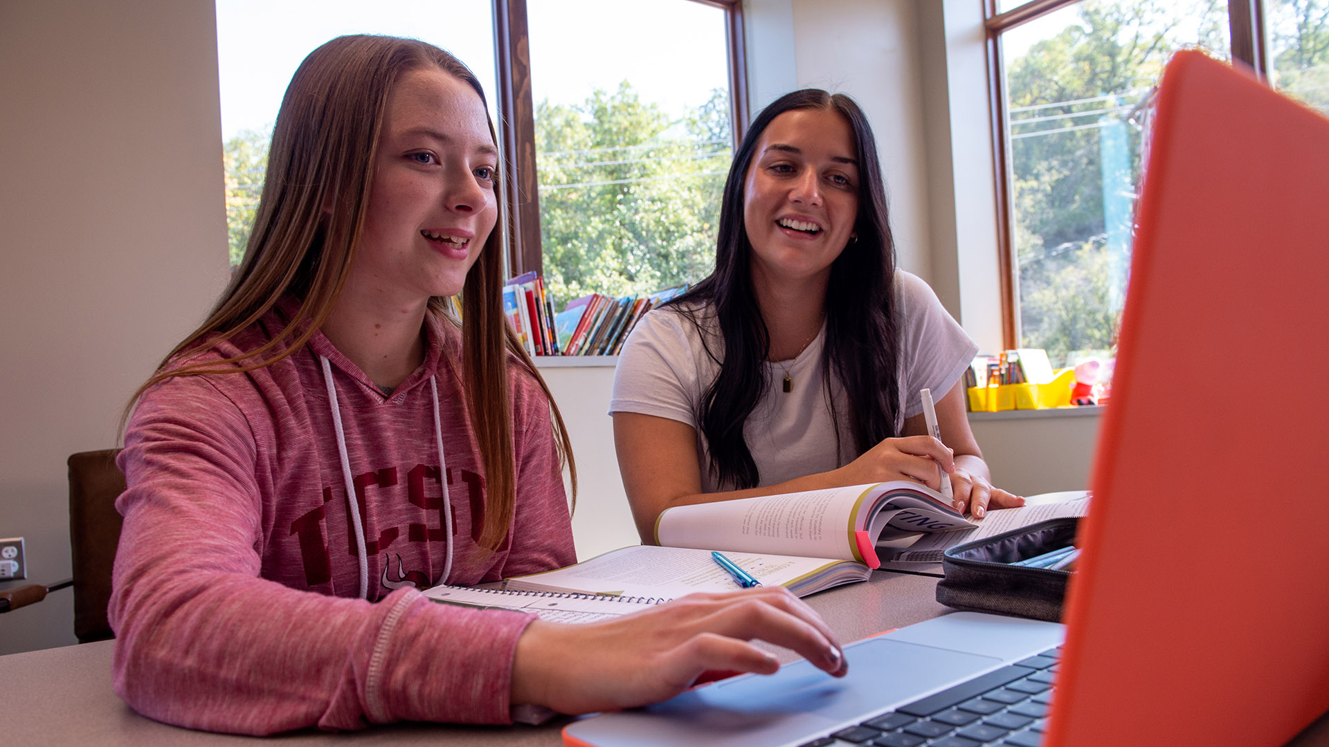 Two female student work at a table with laptops and textbooks