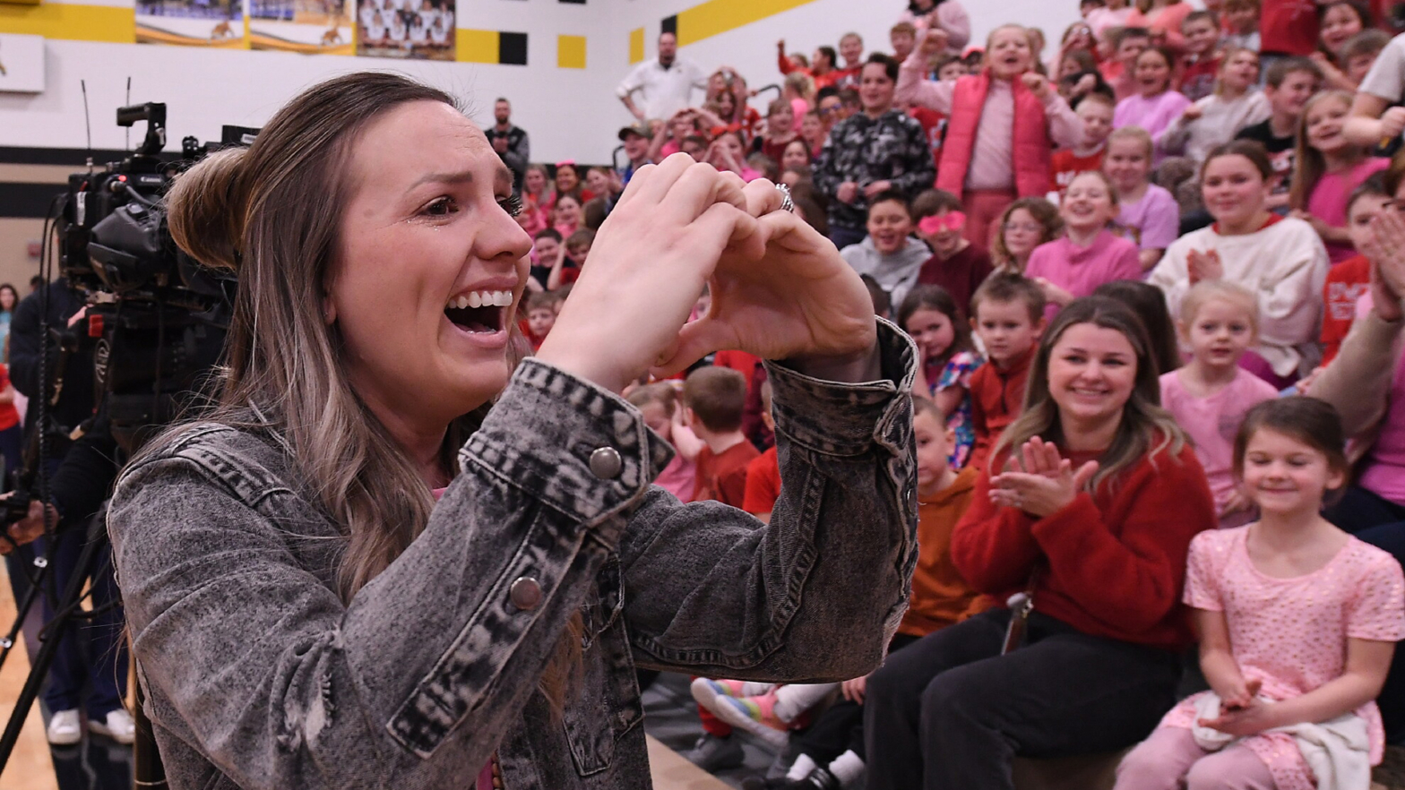 Jessica Stone makes a heart symbol to a crowd of students and staff applauding her Milken Education award.