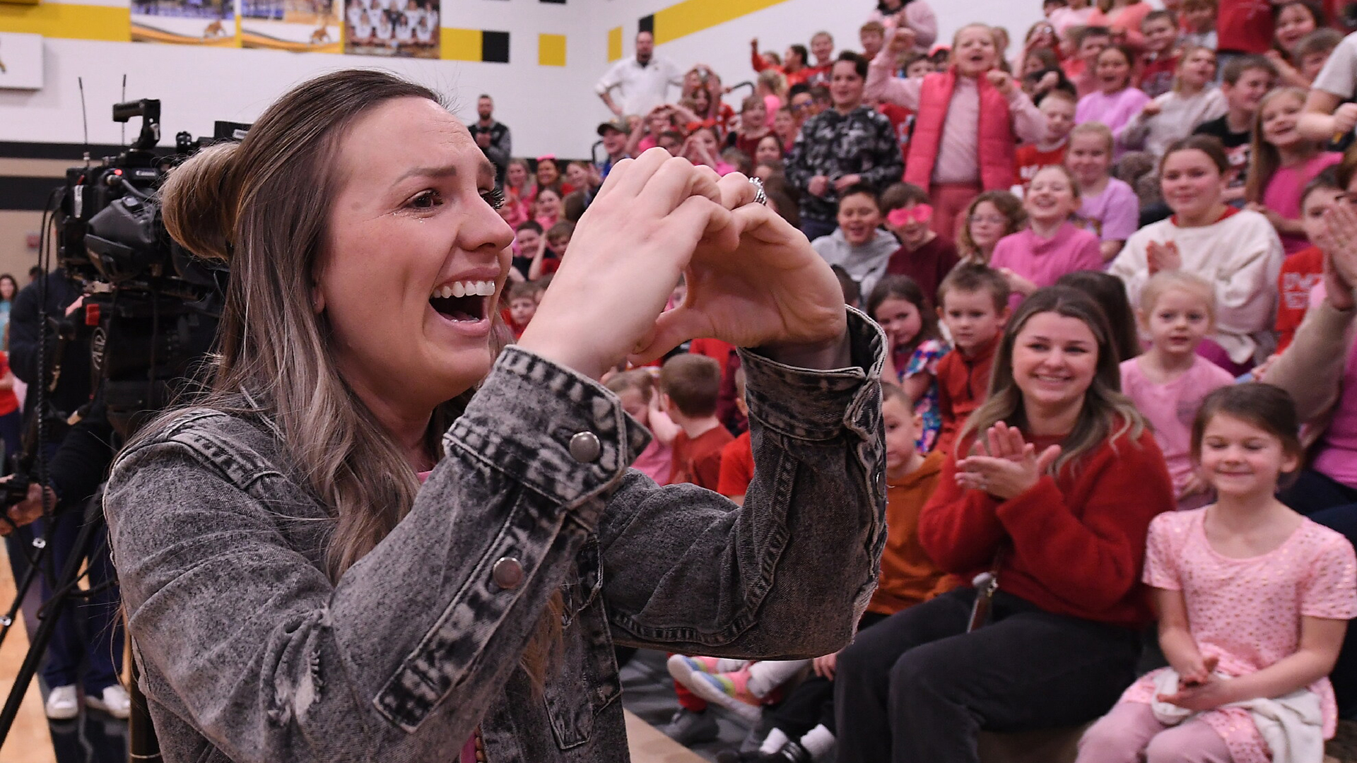 Jessica Stone makes a heart symbol to a crowd of students and staff applauding her Milken Education award.