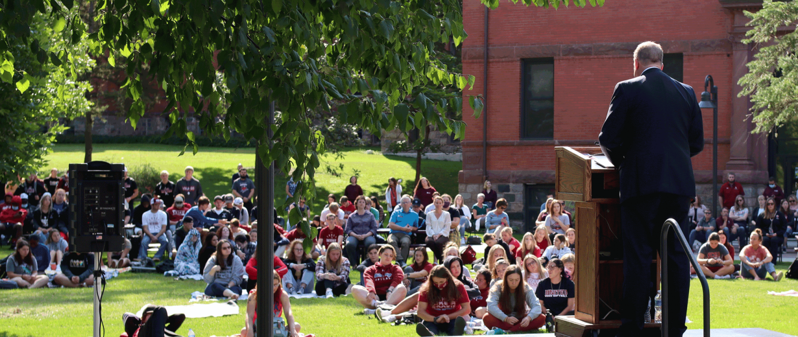 president talking to students and faculty on campus lawn