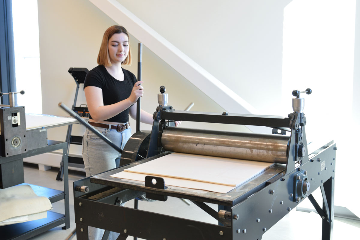 A student runs a printmaking piece of equipment.