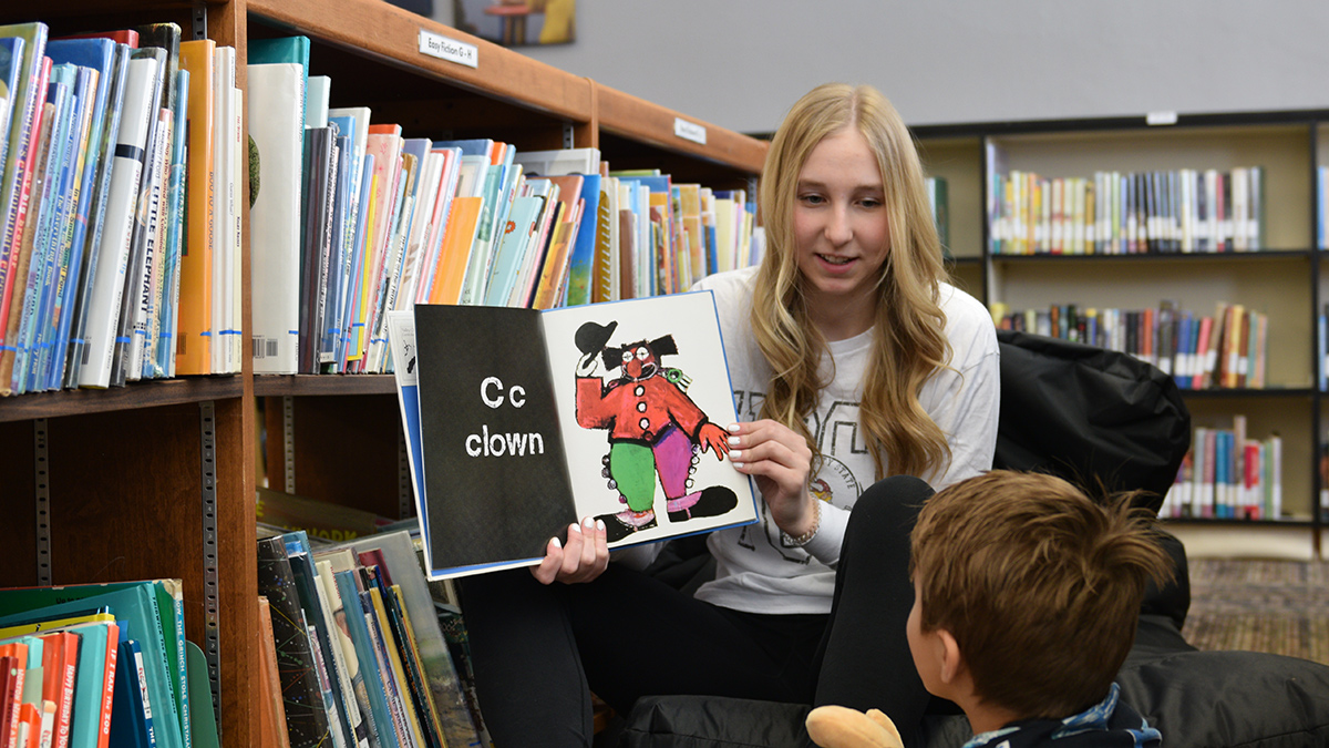 An elementary education major reads to a young student at the library.