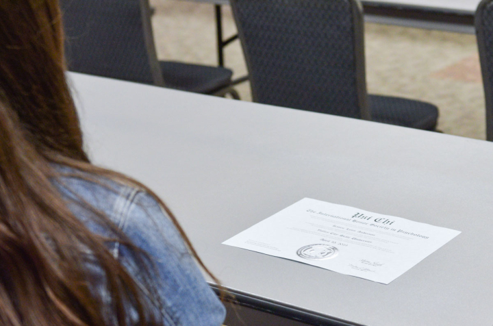 A student sits at a table with a Psi Chi certificate. 