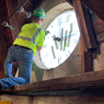 A worker carefully works to prepare the glass from the old clock for removal.