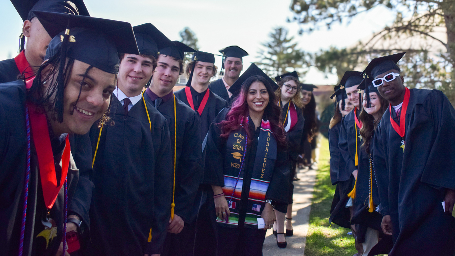 Smiling VCSU students in black caps and gowns wait for the 2024 Commencement to start.