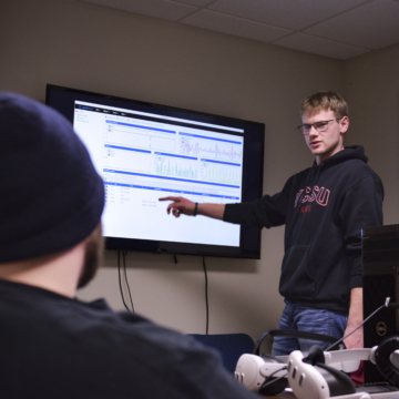 A computer science student presents a PowerBI dashboard to another computer science student who is wearing a stocking hat