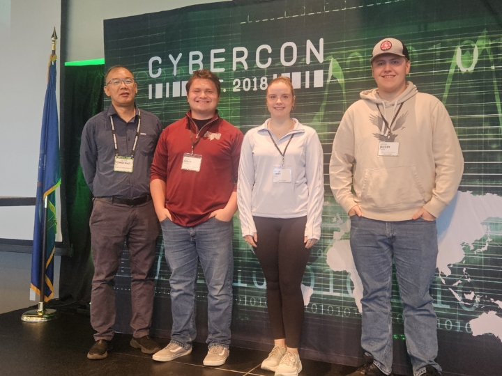 Yongchao and students standing in front of Cybercon backdrop