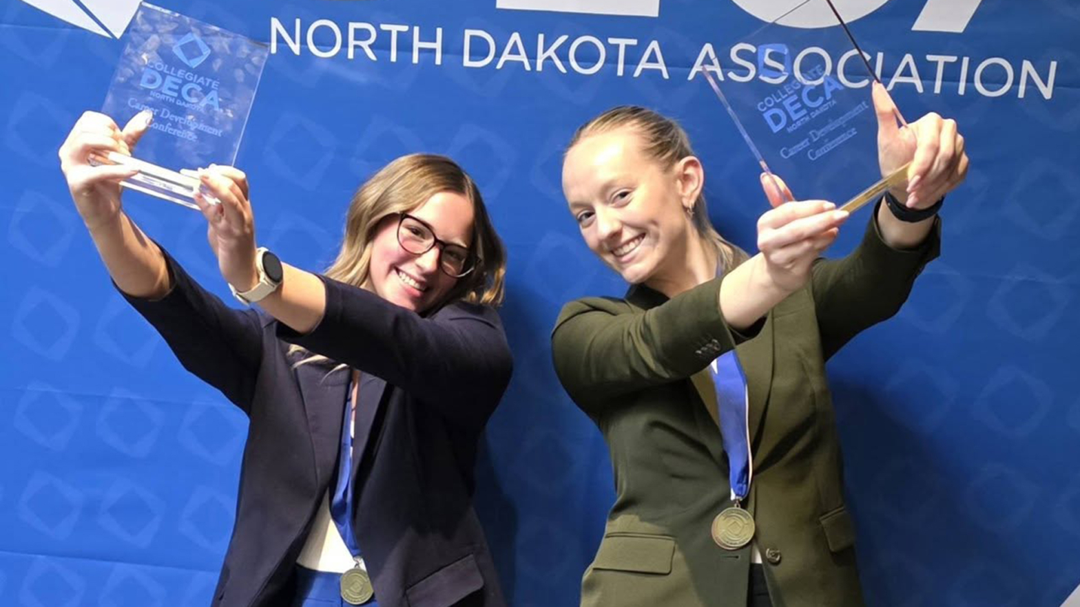 Katie Jones and Sarah Monilaws hold up their championship trophies in front of a blue backdrop