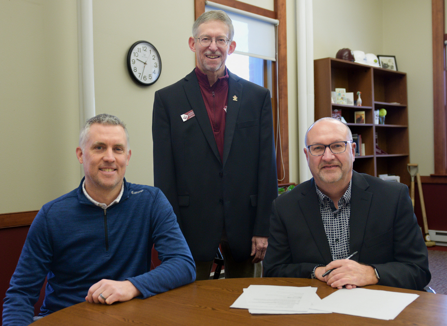 Three VCSU male employees pose for a picture in the President's office. On the table is a signed agreement with UND related to its engineering program