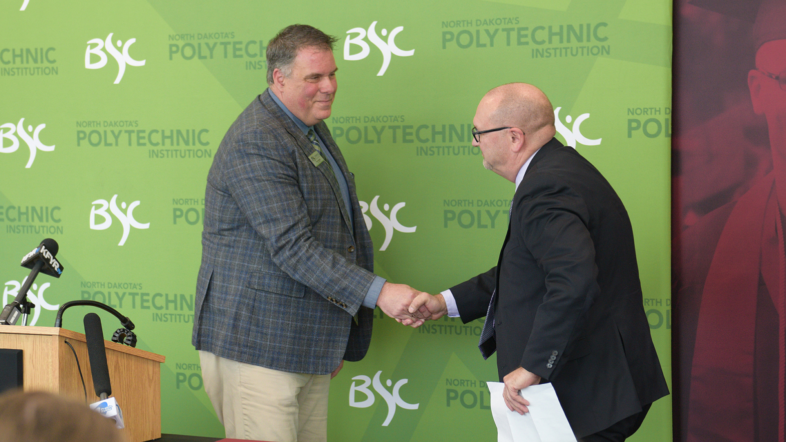Dan Leingang and Allen Burgad shake hands in front of VCSU and BSC backdrops