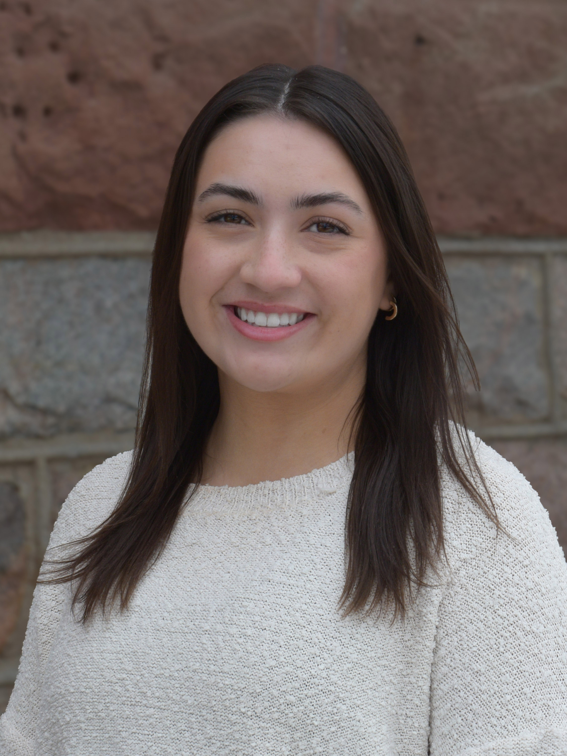 Hanna Wieland stands in front of a brick wall wearing a white sweater