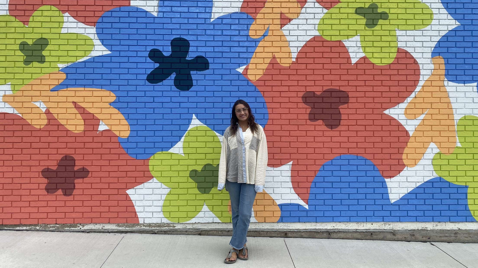 Hanna standing in front of colorful flower wall mural in downtown Valley City