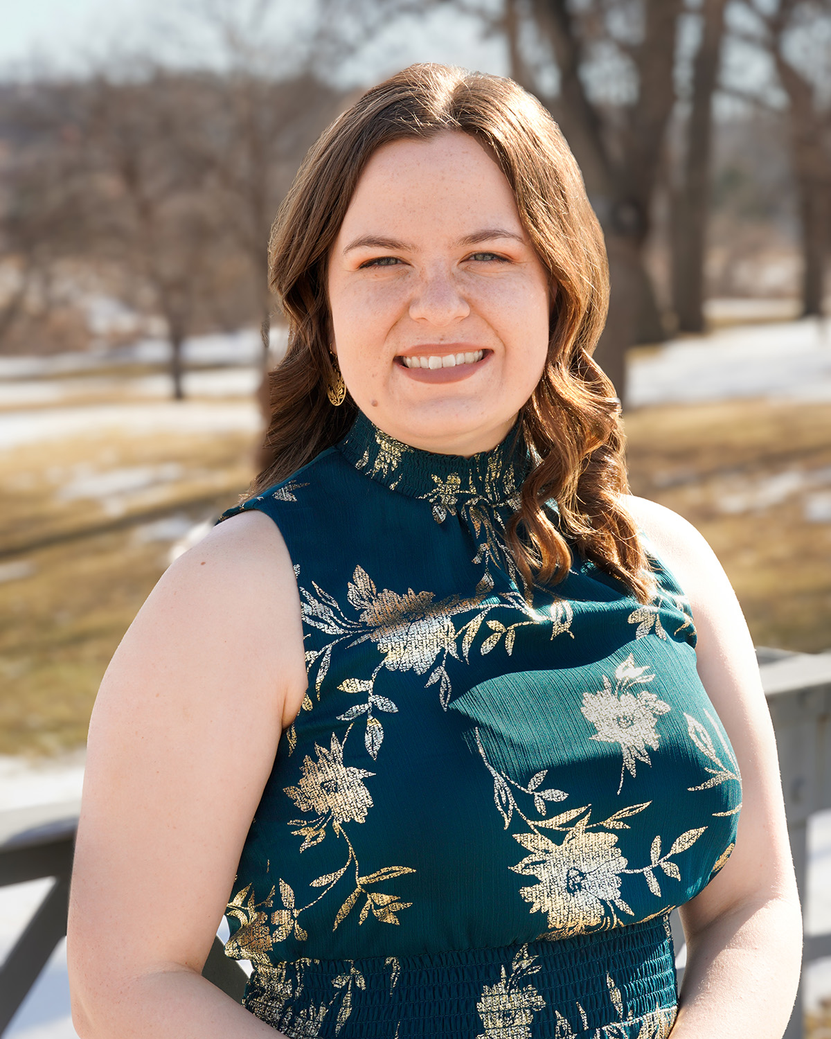 Jora Leeseberg wears a green floral dress while taking a photo outside on a wooden deck.