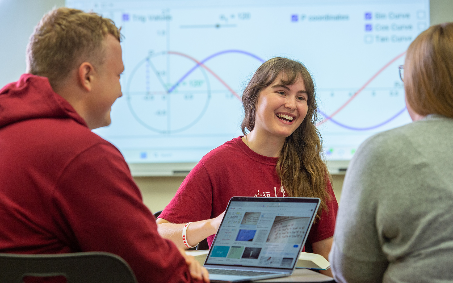 2 math students sit at a table and work closely with a professor of their math class