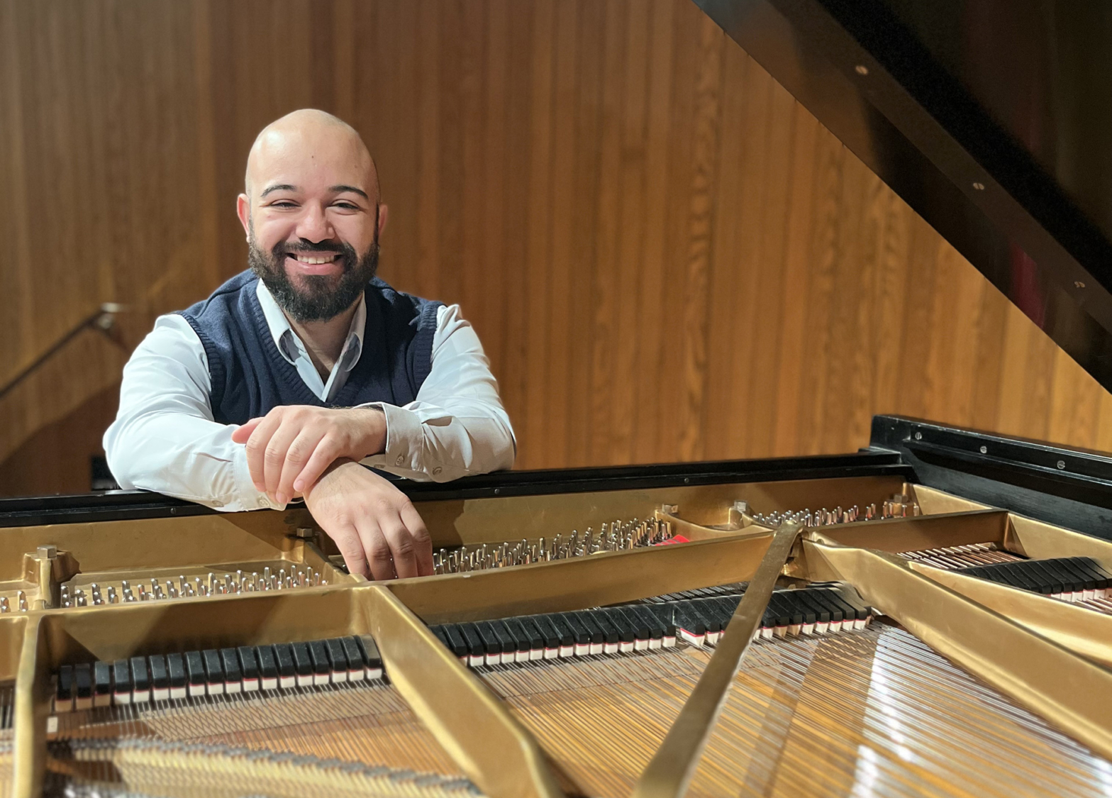 A male pianist stand behind an open piano, exposing the inside of the instrument