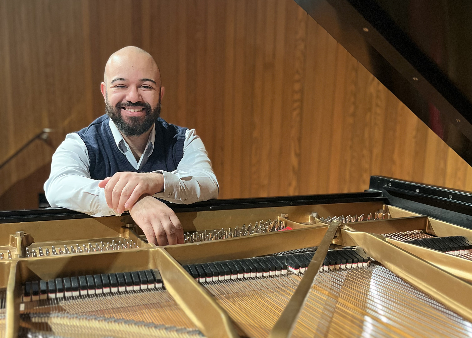 A male pianist stand behind an open piano, exposing the inside of the instrument