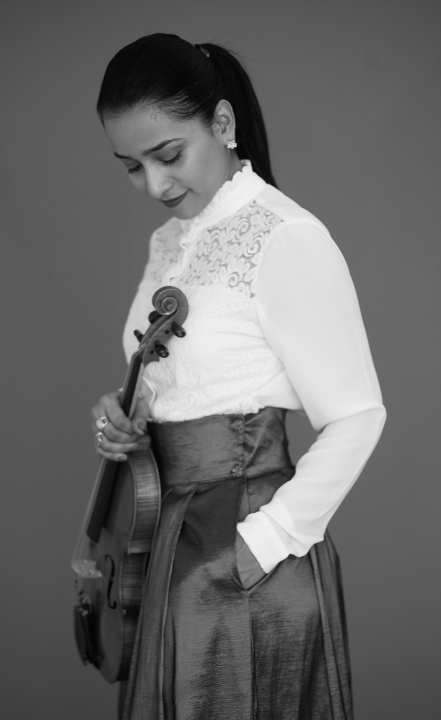 Olga Chavarro stands with her violin in an artistic black and white photo.