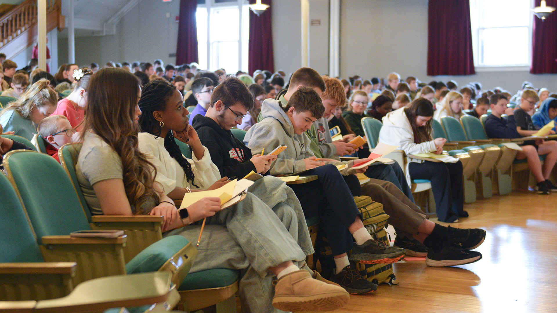 Students gather in an auditorium, working on math questions using paper, pencil and calculators