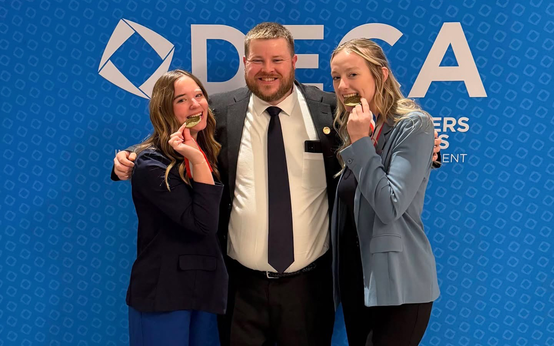 Katie Jones and Sarah Monilaws fake bite their medals while pictured with advisor Wesley Wright