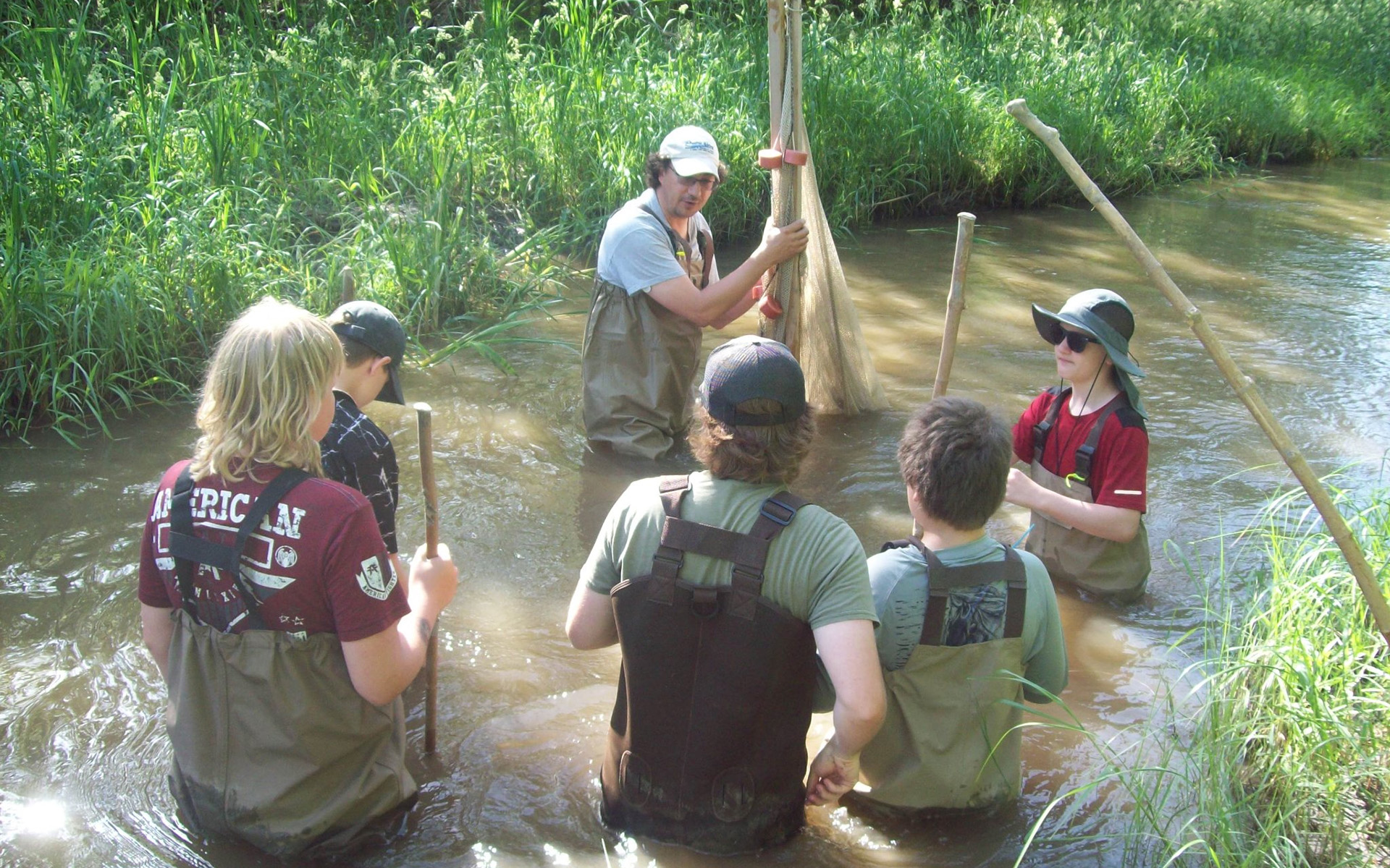 Students wear hip waders as they traverse a small steam during a Prairie Waters camp