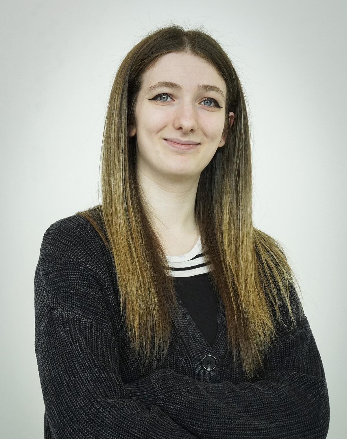 Kara Pranzo smiles at the camera with arms crossed, wearing a black sweater on a white background