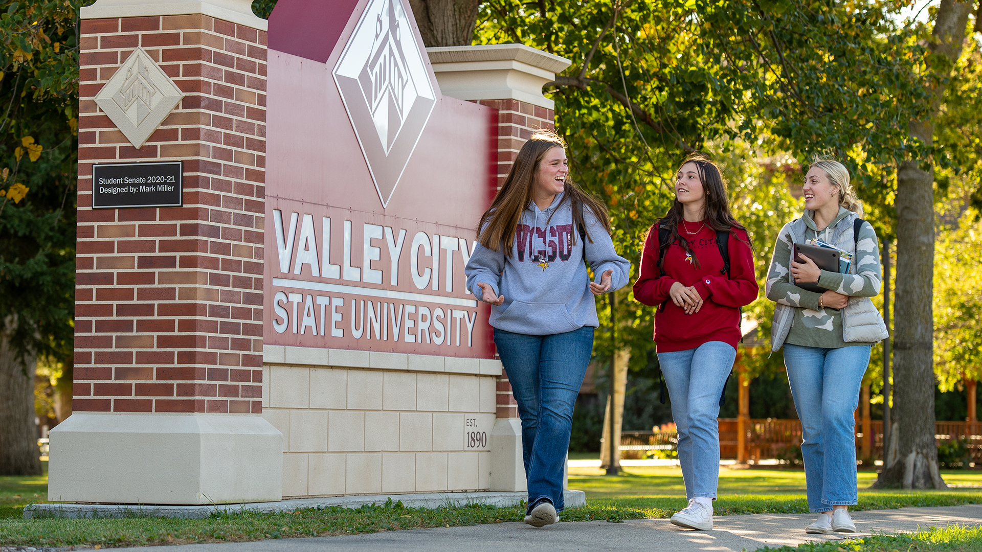 Three female VCSU students walk past a sign that says Valley City State University