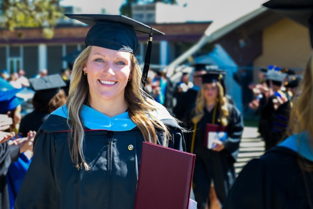 female graduate walking with diploma in hand outdoors