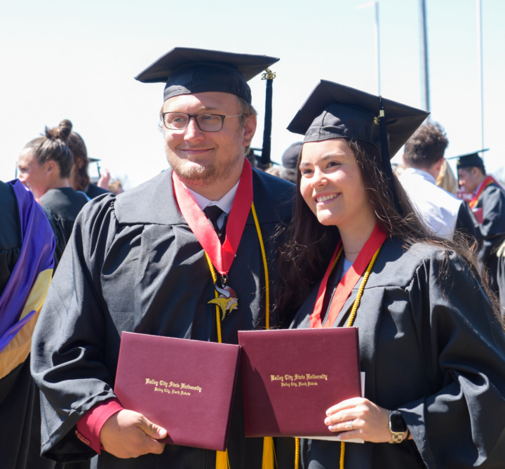 Becca and her fiance at graduation, standing in cap and gown holding diplomas