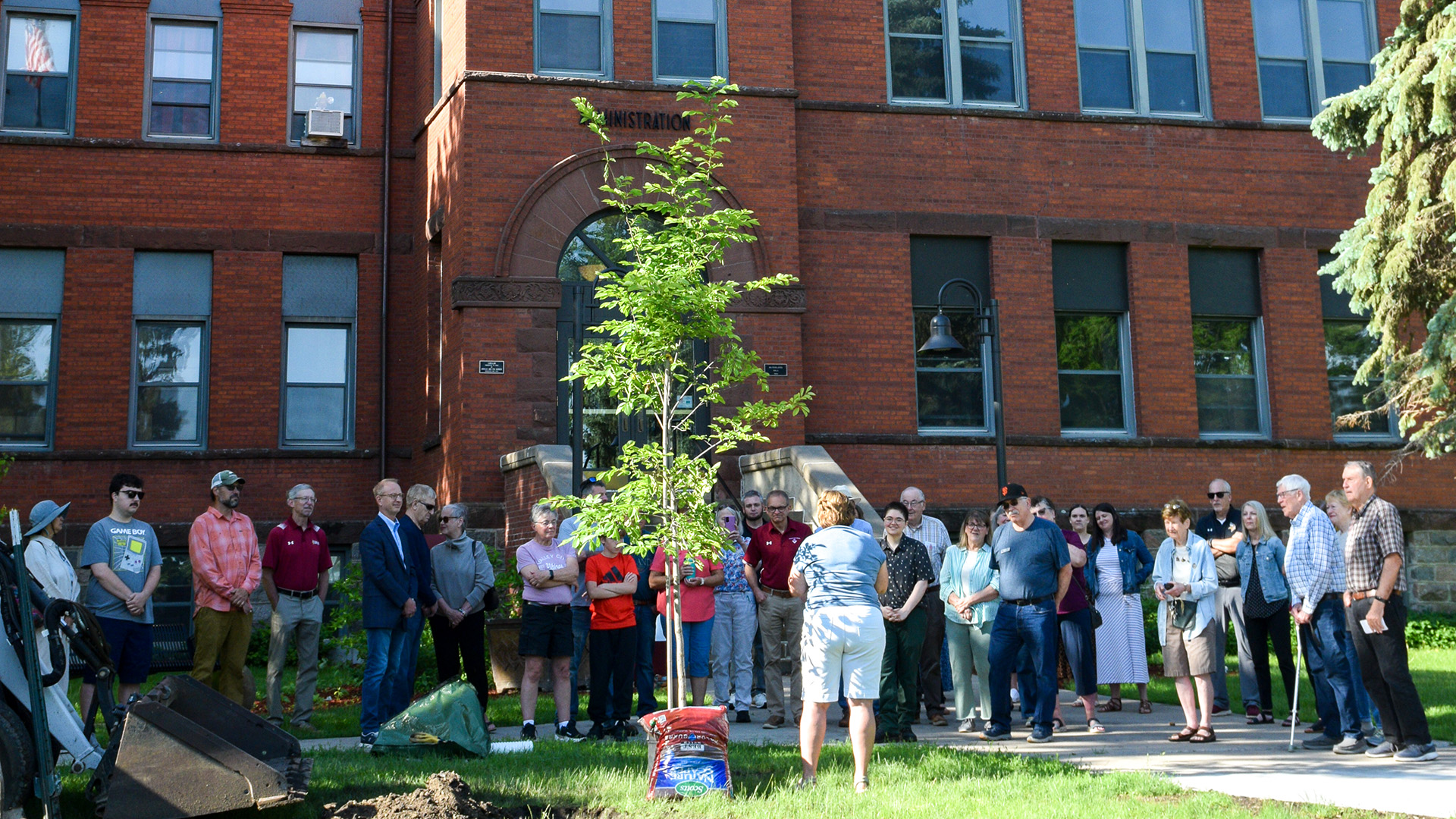 Friends, family and former colleagues gather in front of McFarland Hall and watch as a tree is planted.