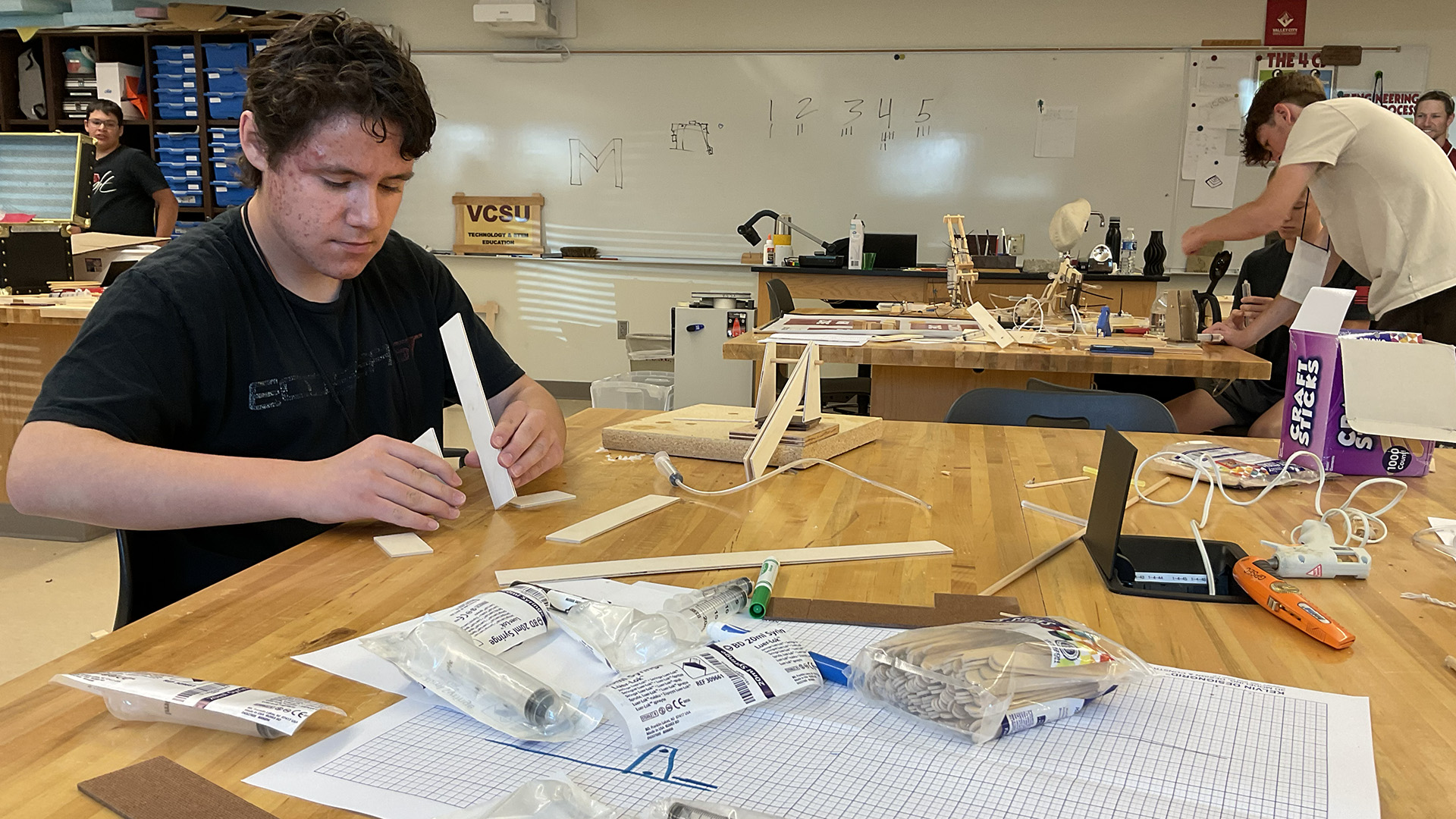 A student works to build a hydraulic arm out of cardboard.
