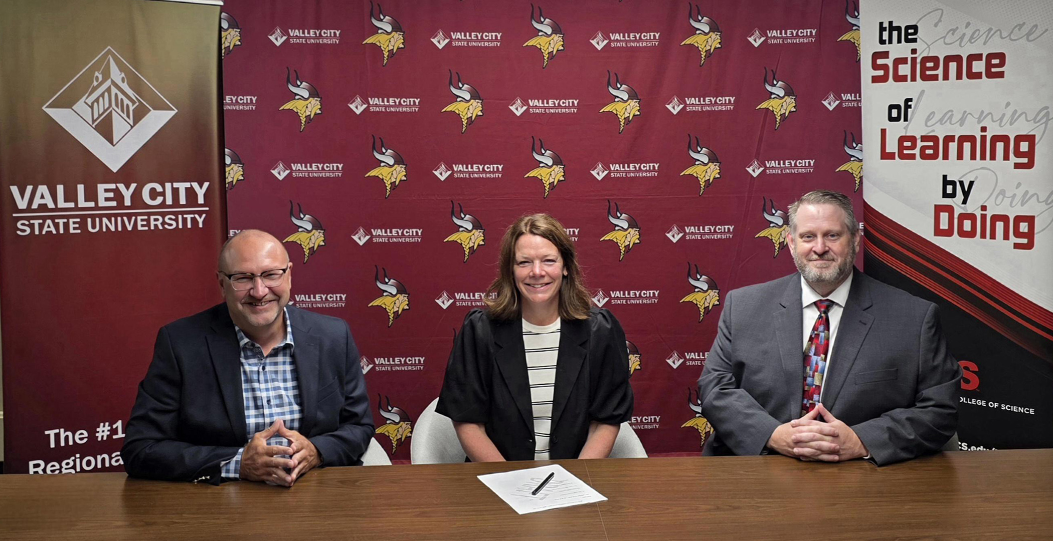 Academic leaders from VCSU and NDSCS sign an agreement in front of VCSU and NDSCS backdrops