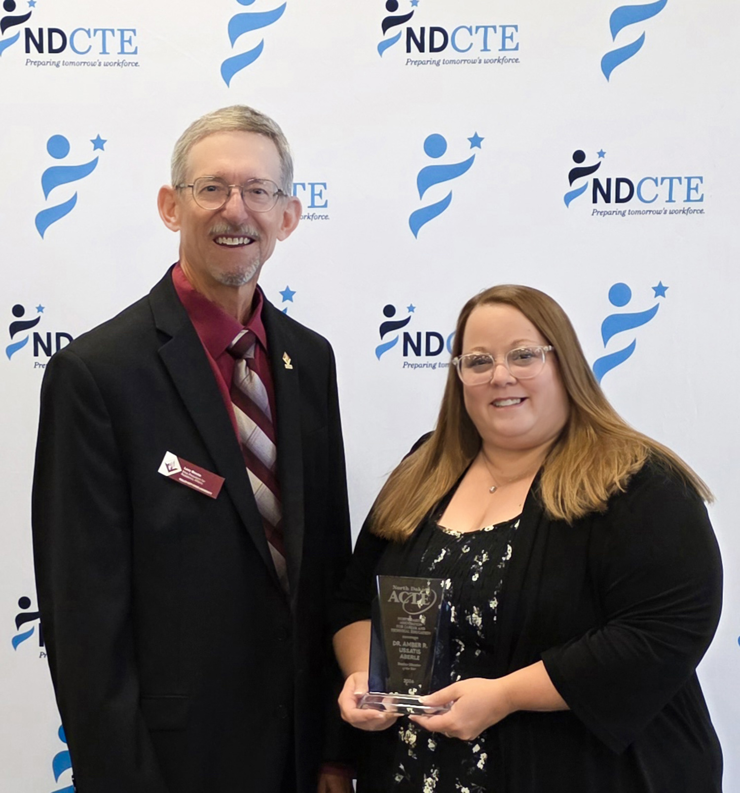 Amber Aberle holds an acrylic award and takes a picture in front of a white backdrop with co-worker Larry Brooks.