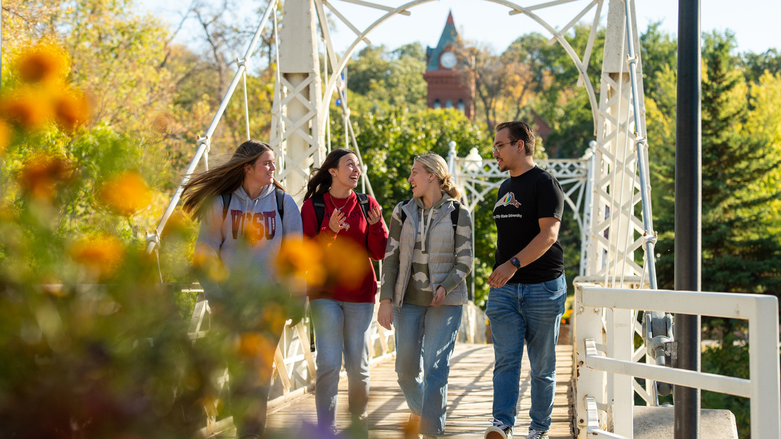 4 student walk across the VCSU walk bridge with the clocktower pictured in the background.