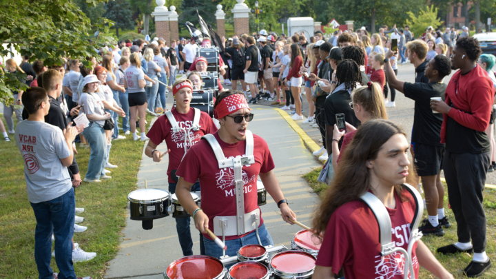 VCSU marching band members play the drums walking through a crowd of VCSU students