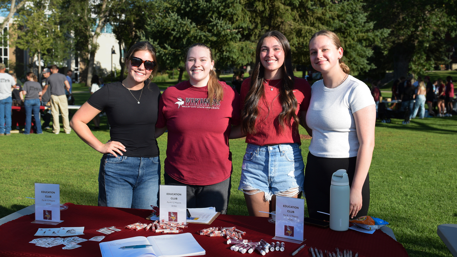 4 VCSU students stand behind a table during the VCSU Marketplace event on the campus front lawn.
