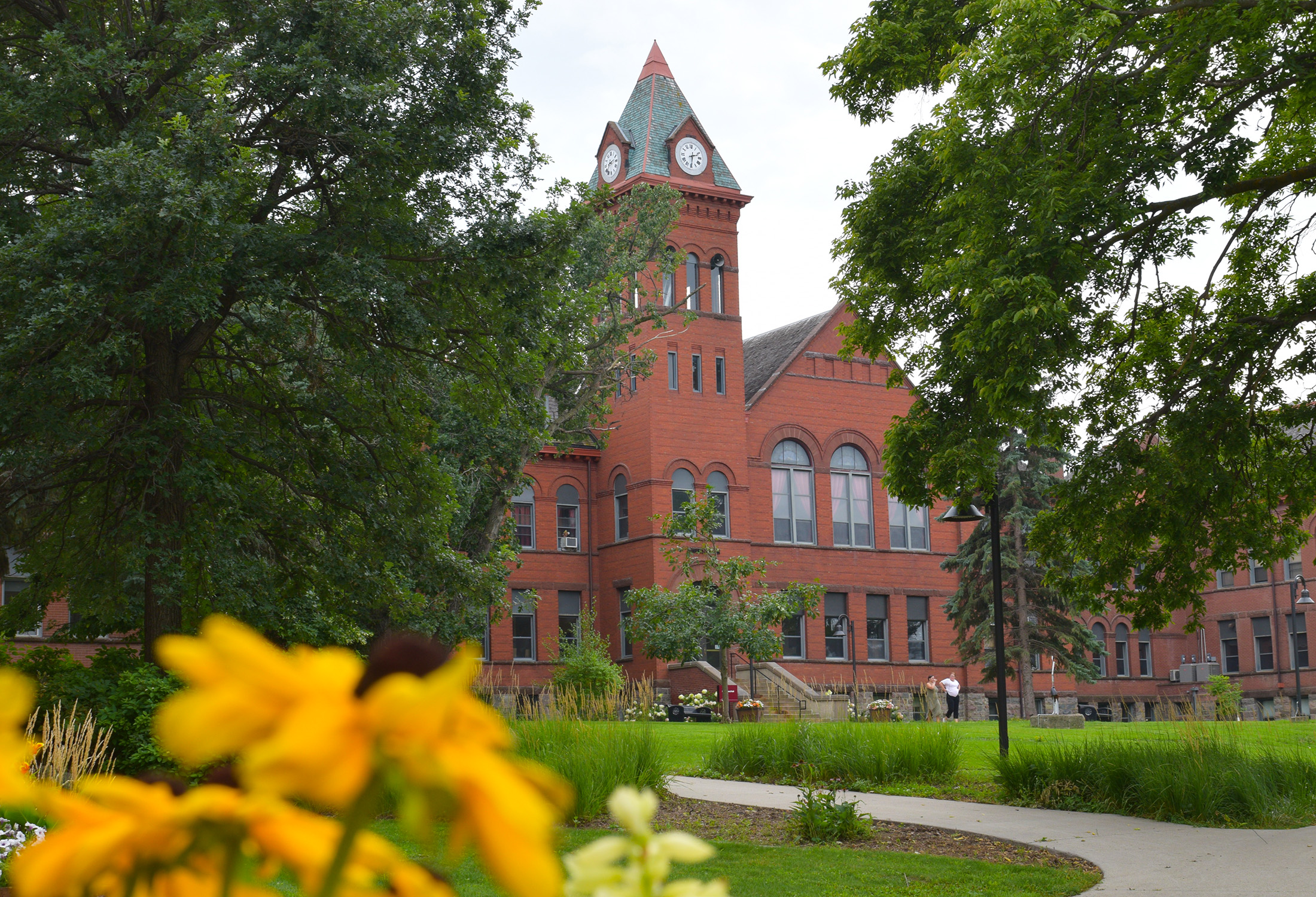 VCSU's McFarland Hall is pictured with green grass and trees and yellow flowers in the foreground