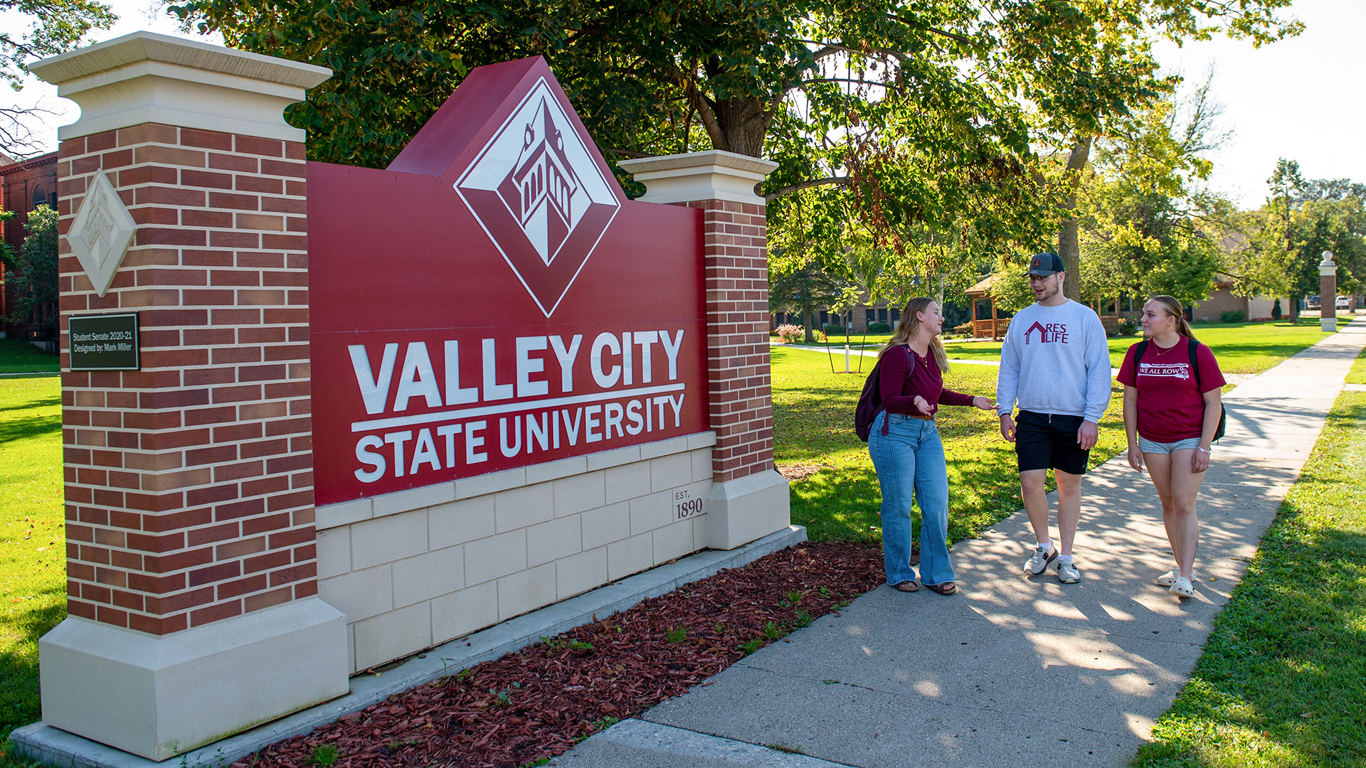 VCSU students walk along a sidewalk near a Valley City State University sign