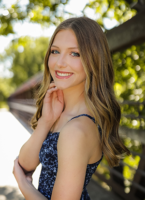 Ann Muggli smiles while posing for a senior photo in front along a sidewalk