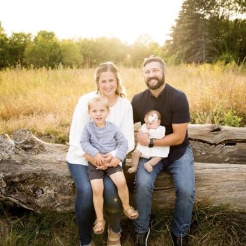 Brittany Foss and family sitting on a log with yellow pasture in the background, smiling for camera
