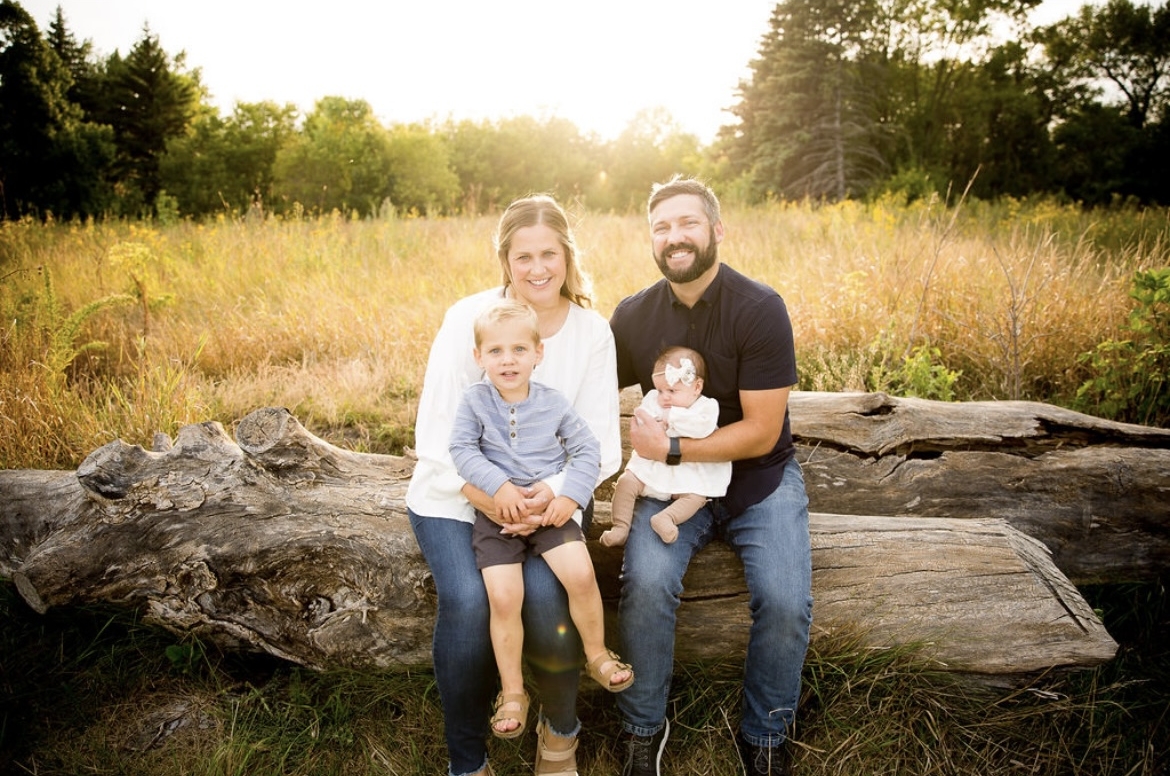 Brittany Foss and family sitting on a log with yellow pasture in the background, smiling for camera