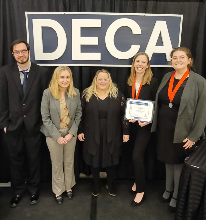 DECA students standing by DECA sign