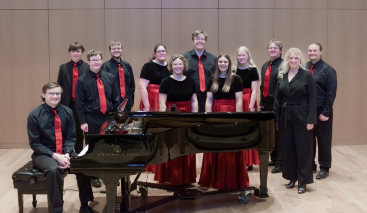 Photo of choir dressed in black and red with grand piano in foreground