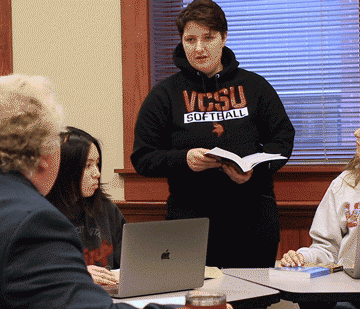 An english student holds a book and leads a group discussion.