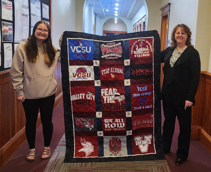 Piper Hanna and Kerry Gregoryk with hold up Kerry's handmade quilt for the live auction