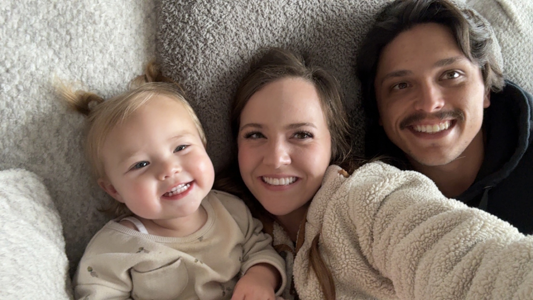 Sydni Smith smiling at the camera with her daughter and husband
